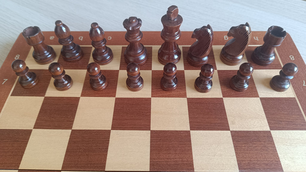 Rangée complète des pièces d'échecs foncées aimantées sur l'échiquier en bois